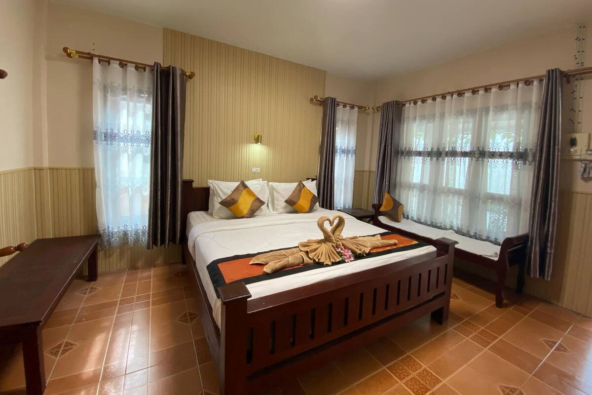 A hotel room with a large bed, two bedside tables, a bench, and a wall-mounted light.