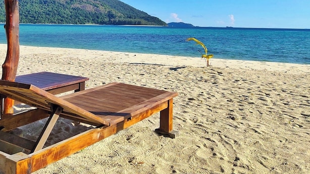 Une plage avec un fauteuil de plage en bois et un parasol en chaume.