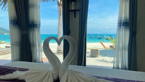 Un lit agrémenté d’une décoration en forme de cœur faite avec des serviettes, et donnant sur une plage où se trouvent des bateaux.