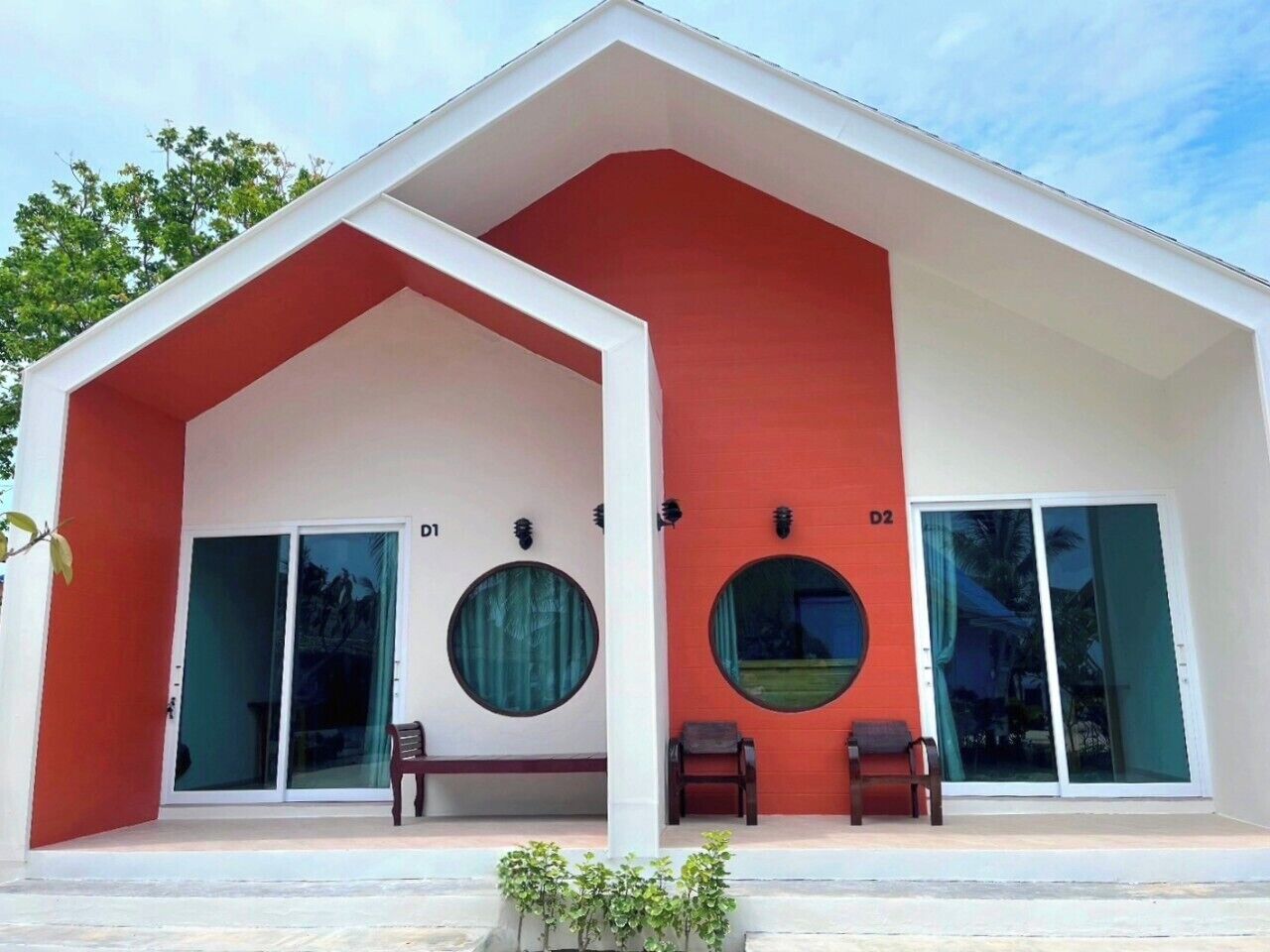 Un edificio moderno con una paleta de colores rojo y blanco, que presenta dos grandes ventanas con cortinas, un banco y una pequeña mesa.