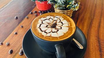A cup of coffee with latte art on a wooden table, surrounded by coffee beans and small Christmas trees.
