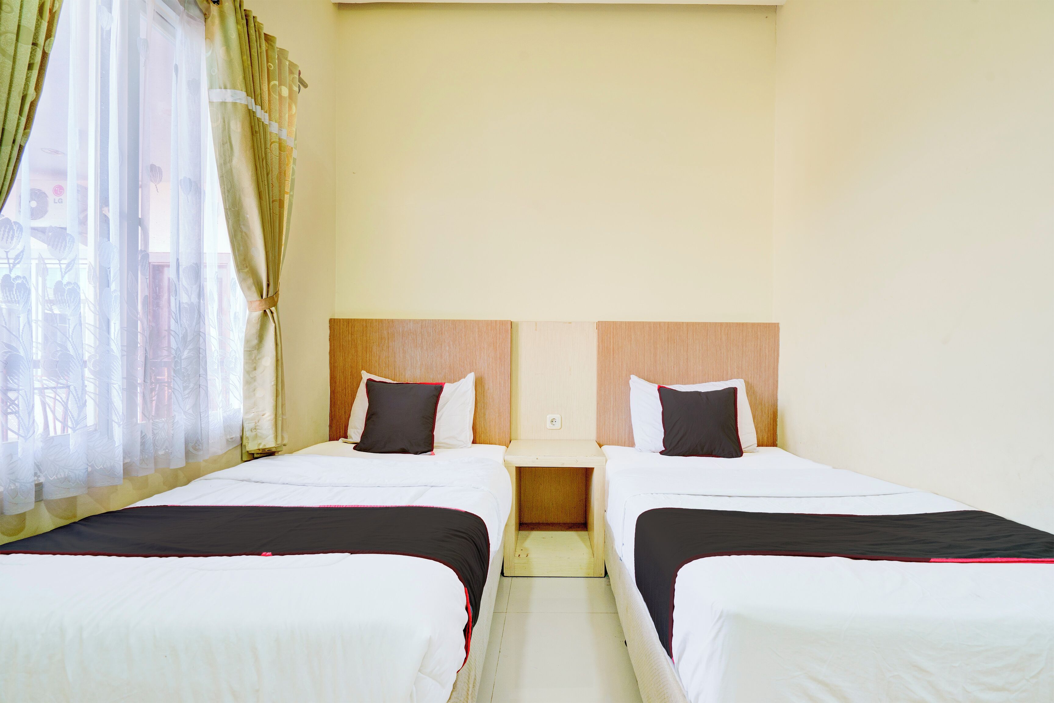A hotel room with two beds, each with a pillow and a bedside table.