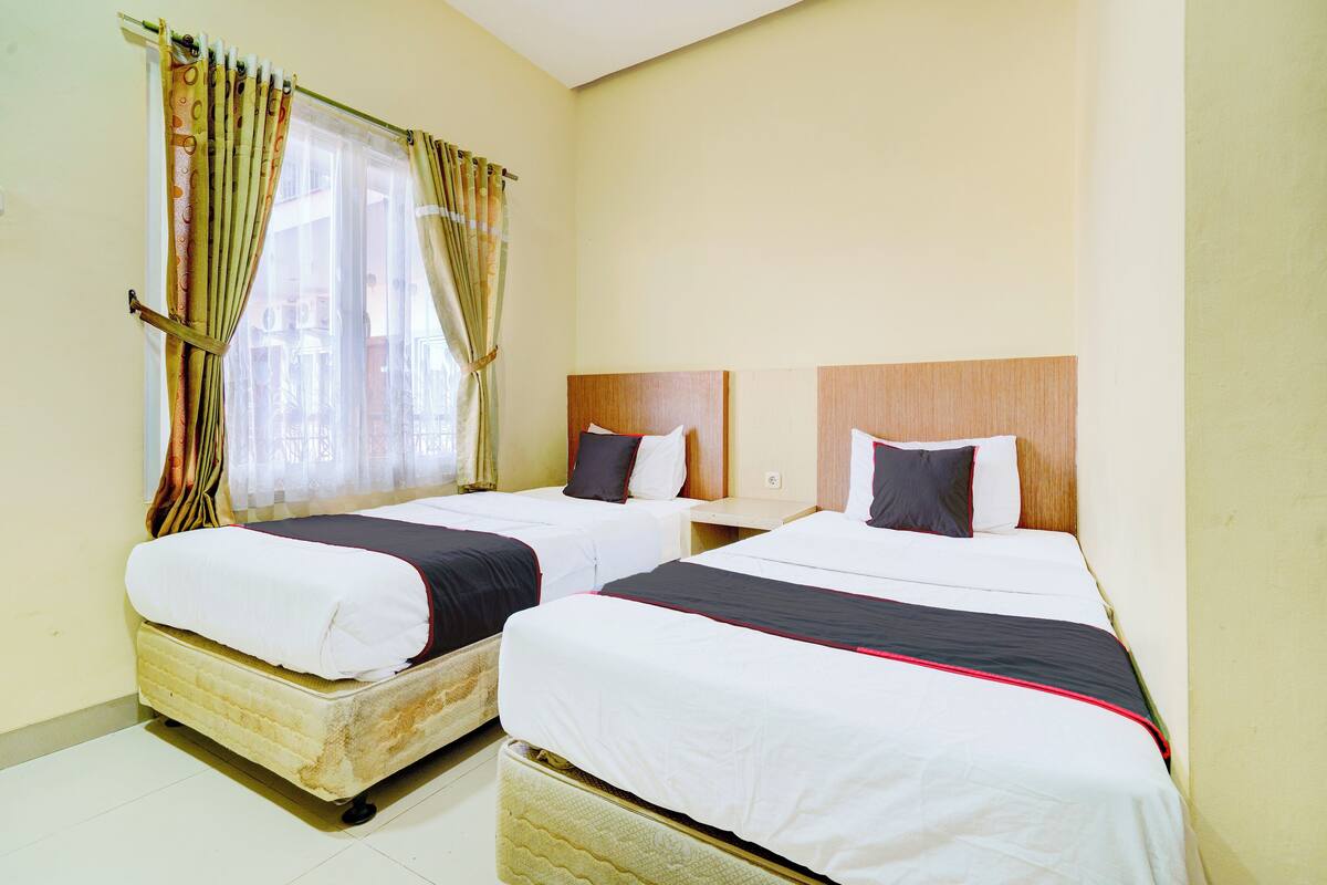 A hotel room with two beds, a wooden headboard, and a window with curtains.