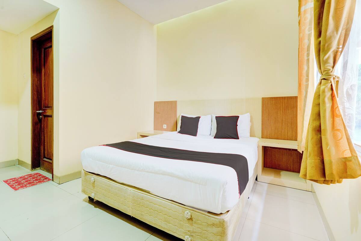 A bedroom with a bed, a nightstand, a wooden headboard, a red rug, and a door.