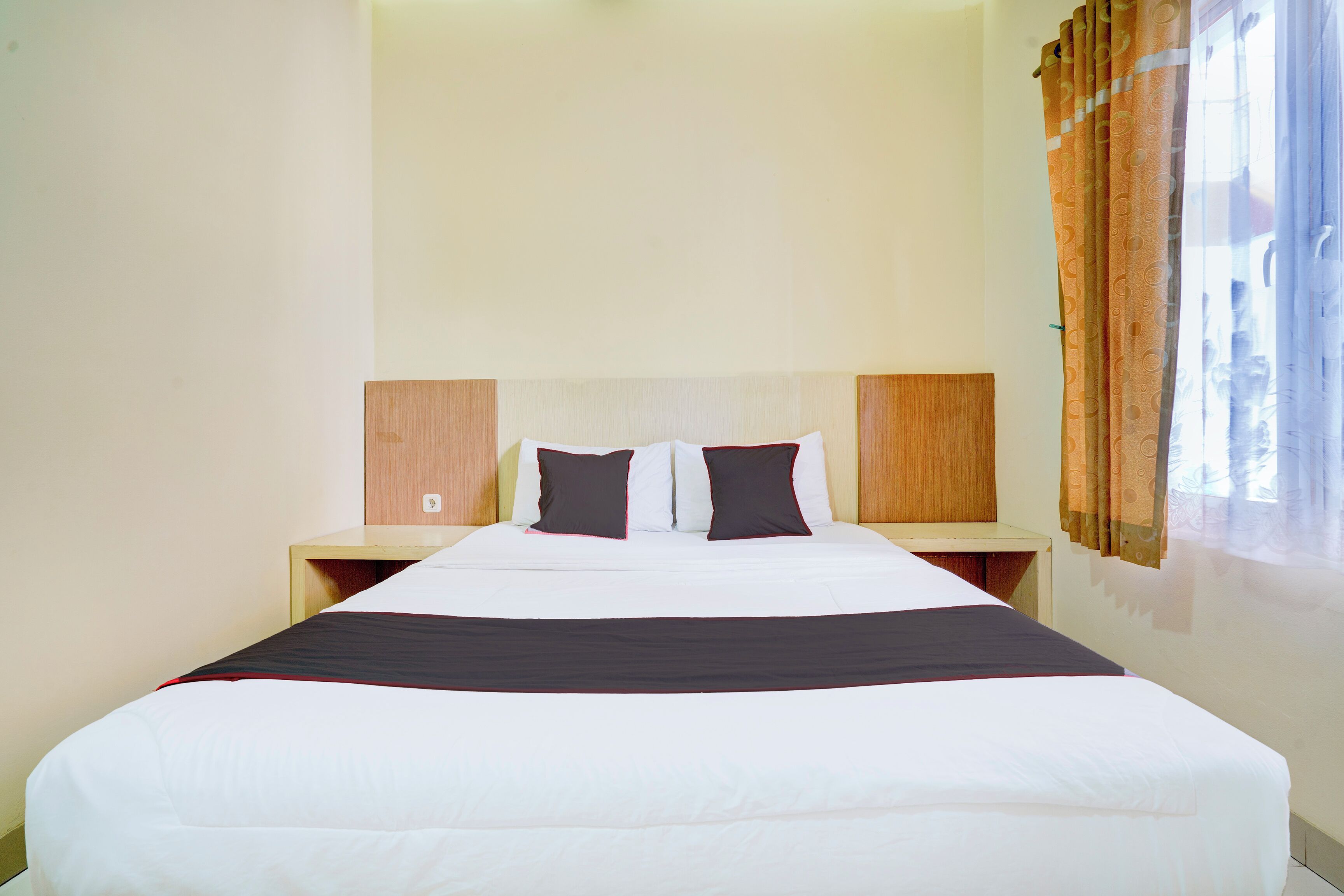 A hotel room with a large bed, two bedside tables, and a window with curtains.