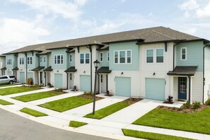 A row of townhouses with individual garages, a well-maintained lawn, and a clear sky.