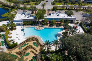 An aerial view of a resort with a large pool, palm trees, and a parking area.