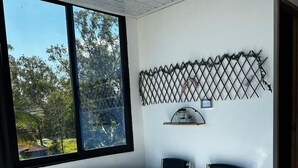 A modern bathroom with a large freestanding bathtub, a window with a view of trees, and a decorative metal shelf with a small plant. - Hotel Mirador Cielo Blue-20Min Guatapé. (El Peñol)