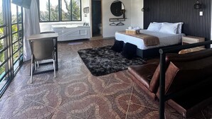 A modern bedroom with a large bed, a desk, and a chair. There is a window with a view of trees and a balcony. - Hotel Mirador Cielo Blue-20Min Guatapé. (El Peñol)