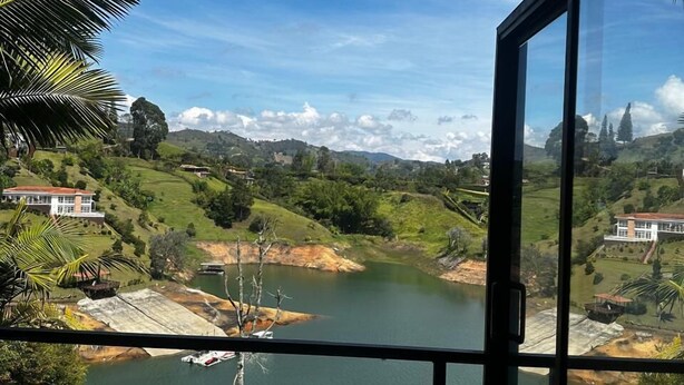 A view from a window overlooking a lake, surrounded by greenery and hills. - Hotel Mirador Cielo Blue-20Min Guatapé. (El Peñol)