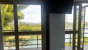 A bedroom with a bed, a TV mounted on the wall, and large windows offering a view of a lake and greenery. - Hotel Mirador Cielo Blue-20Min Guatapé. (El Peñol)