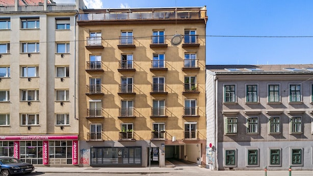 A multi-story building with a ground-level entrance, multiple balconies, and a visible storefront with signage.