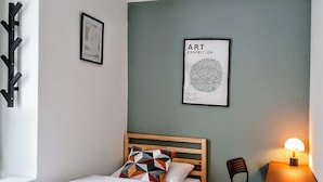 A neatly made bed with a geometric pillow, a small table with a lamp, and a framed artwork on the wall.