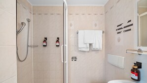 A bathroom with a shower, toilet, and sink. There are two bottles of soap on the wall. - Flora Collections - Studio room with shared kitchen (Vienna)