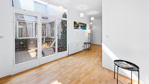 A bright hallway with wooden flooring, a glass door leading to an outdoor area, and a small table with a magazine. - Flora Collections - Studio room with shared kitchen (Vienna)