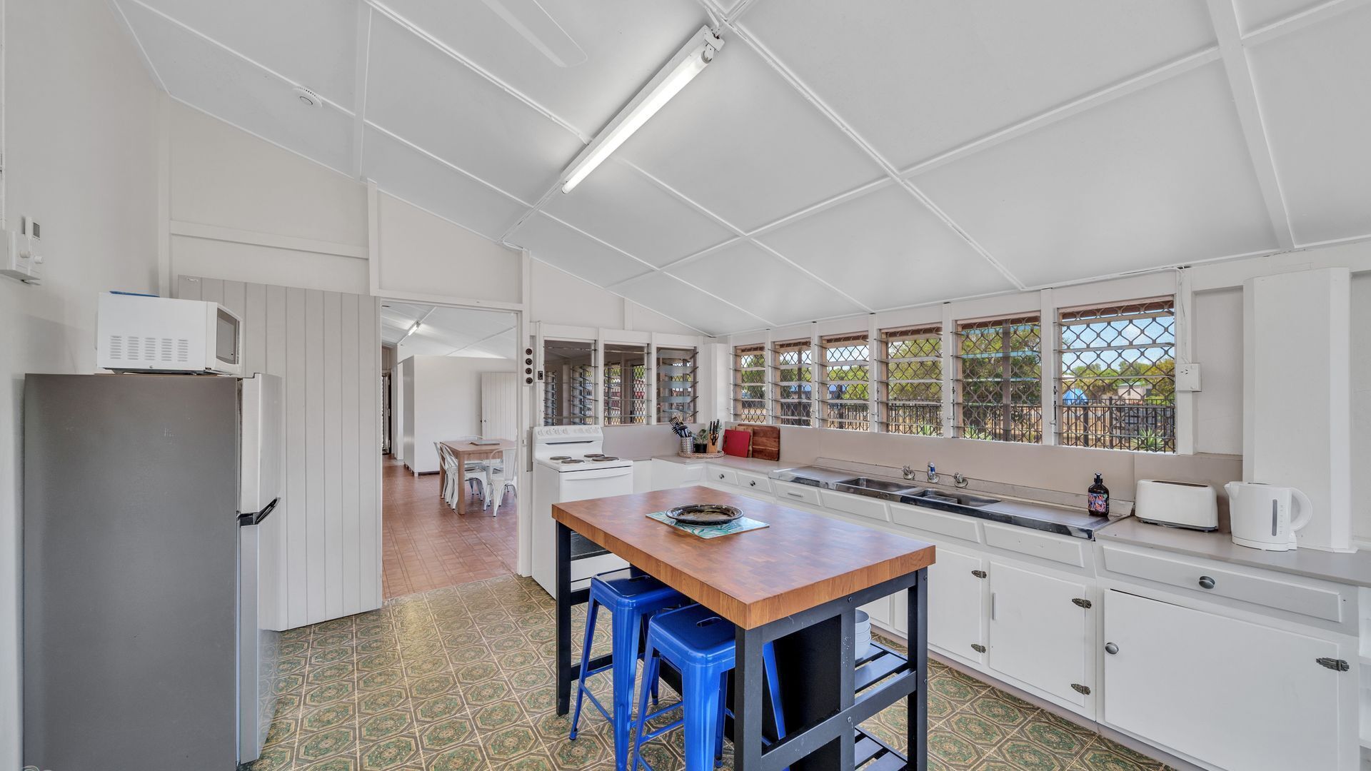 Une cuisine moderne avec des meubles blancs, un îlot central en bois, des tabourets de bar bleus et une vue par la fenêtre.