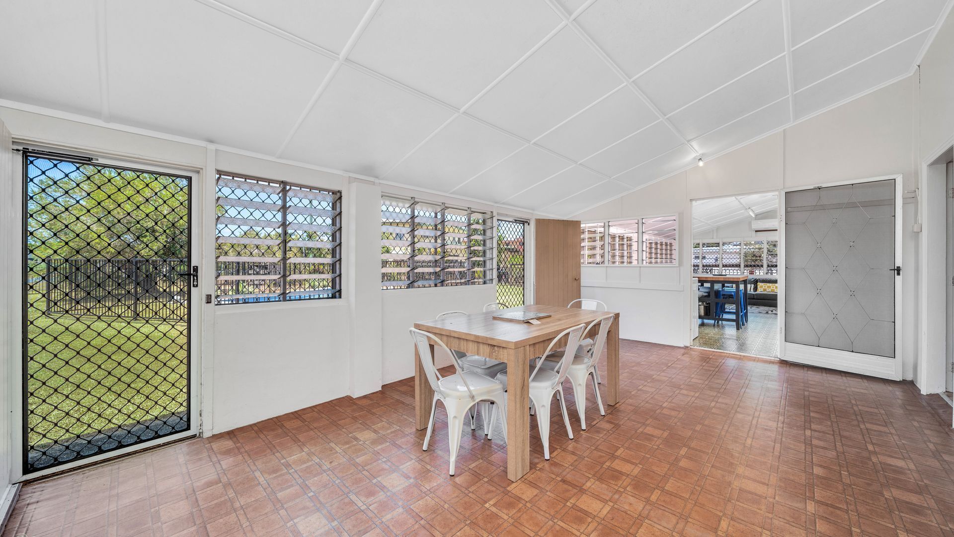 Une pièce spacieuse avec une table à manger en bois, des chaises blanches et une vue par les fenêtres.
