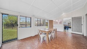 Una habitación amplia con una mesa de comedor de madera, sillas blancas y vistas por las ventanas.