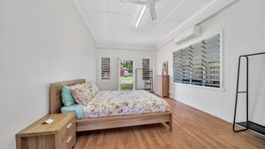 Un dormitorio con cama de madera, mesita de noche, cómoda, ventana con persianas y ventilador de techo.