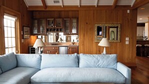 A living room with a light blue sofa, wooden walls, and a kitchen in the background.