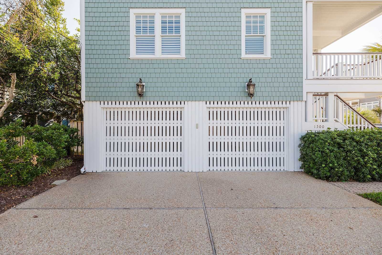 Una casa de dos pisos con fachada azul claro, puertas de garaje blancas y un pequeño balcón en el segundo piso.