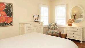 A bedroom with a bed, two nightstands, a chair, a dresser, a mirror, and a framed picture on the wall.