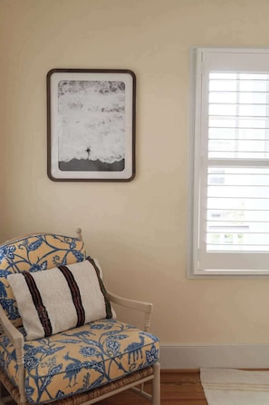 A room with a chair, a framed picture on the wall, and a window with blinds. - The Holiday | 5BR 5BA Coastal Retreat (Wrightsville Beach)