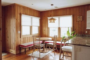 A wooden-paneled room with a round table, two chairs, a bench, and a hanging light fixture.