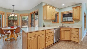 A kitchen with wooden cabinets, a dishwasher, and a dining area with a table and chairs. - Bluebird Song | Prime Flagstaff Location | Outdoor Retreat with Fenced Yard and Firepit (Flagstaff)