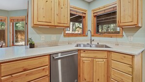 A kitchen with wooden cabinets, a stainless steel dishwasher, and a window with a view of the outdoors. - Bluebird Song | Prime Flagstaff Location | Outdoor Retreat with Fenced Yard and Firepit (Flagstaff)