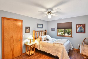 A bedroom with a wooden bed, a nightstand with a lamp, a ceiling fan, and framed pictures on the walls. - BunnyLand Lodge | Panoramic Mt. Views | Fantastic Backyard Patio | Scenic Location in Flagstaff (Flagstaff)