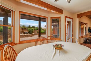 A dining area with a round table, wooden chairs, and large windows offering a view of a landscaped garden. - BunnyLand Lodge | Panoramic Mt. Views | Fantastic Backyard Patio | Scenic Location in Flagstaff (Flagstaff)