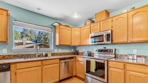 A kitchen with wooden cabinets, stainless steel appliances, a window with a view of trees, and a granite countertop. - ACE - A Hole in One! | Right on the Golf Course | Hot Tub |  Mt Views & Pines (Flagstaff)