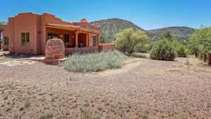 Una casa de estuco con chimenea de ladrillo, un patio y vista a la montaña.