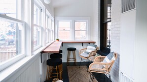 A narrow, white-walled room with a wooden bench and two wicker chairs, a small table, and a radiator. - Doc's Place | Historic Jewel In Downtown Flagstaff | Sophisticated Elegance (Flagstaff)