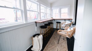 A kitchen with white walls, large windows, bar stools, wicker chairs, and a wooden countertop. - Doc's Place | Historic Jewel In Downtown Flagstaff | Sophisticated Elegance (Flagstaff)