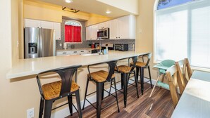 A modern kitchen with a central island, bar stools, and a dining area with a table and chairs. - Mountain Jewel | Modern Townhome in the Pines | Great Location | Near Downtown Flagstaff (Flagstaff)