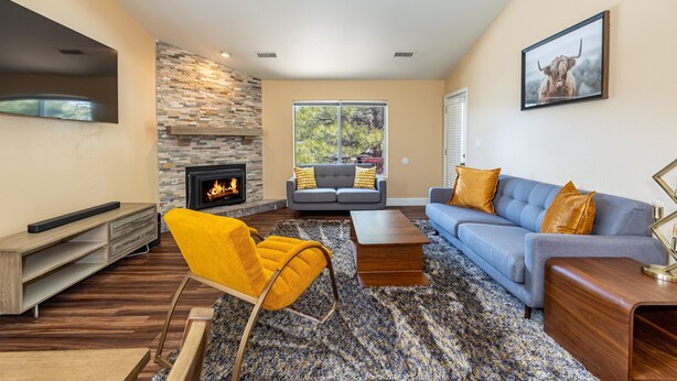 A modern living room with a fireplace, a sofa, a yellow chair, and a television. - Mountain Jewel | Modern Townhome in the Pines | Great Location | Near Downtown Flagstaff (Flagstaff)