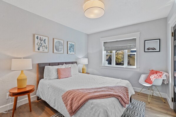 A bedroom with a bed, bedside tables, a window, and artwork on the wall.