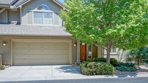 Une maison d’habitation avec un garage beige, une porte d’entrée et un arbre dans le jardin.