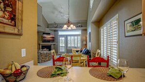 Un coin repas avec une table dressée pour deux personnes, un panier de fruits et un verre à vin.