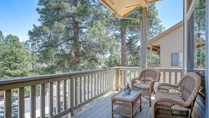Une terrasse extérieure couverte, aménagée avec des meubles en osier, une table et offrant une vue sur les arbres environnants.