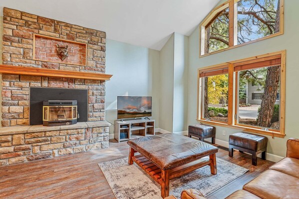 A living room with a stone fireplace, a television, and a large window with a view of trees.