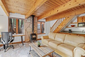 A cozy living room with a stone fireplace, a sofa, a coffee table, and a desk with a chair.