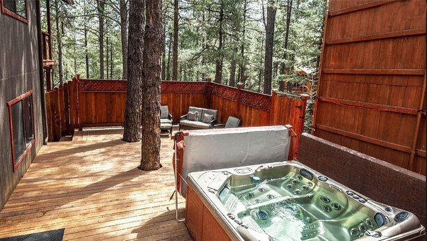 A wooden deck with a hot tub, seating area, and a view of the forest. - Eternal Treehouse | Hot Tub, Outdoor Paradise, Entertainment & Scenic Pine Views (Flagstaff)