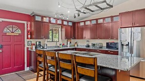 A modern kitchen with granite countertops, stainless steel appliances, and wooden chairs. - Eternal Treehouse | Hot Tub, Outdoor Paradise, Entertainment & Scenic Pine Views (Flagstaff)