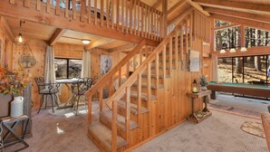 A wooden interior with a staircase, a pool table, and a dining area with a view of the outdoors.
