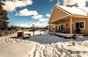 Un'area esterna innevata con un edificio in legno, un recinto e un piccolo albero.