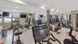 A gym with various exercise equipment, a television screen, and large windows.