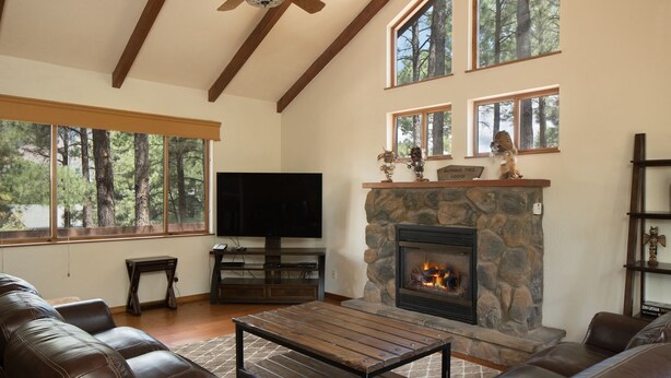 A living room with a stone fireplace, leather sofas, a wooden coffee table, and a flat-screen TV. - Burning Tree Lodge - Forest Views, Fire Pit, AC | Pet and Family Friendly (Flagstaff)